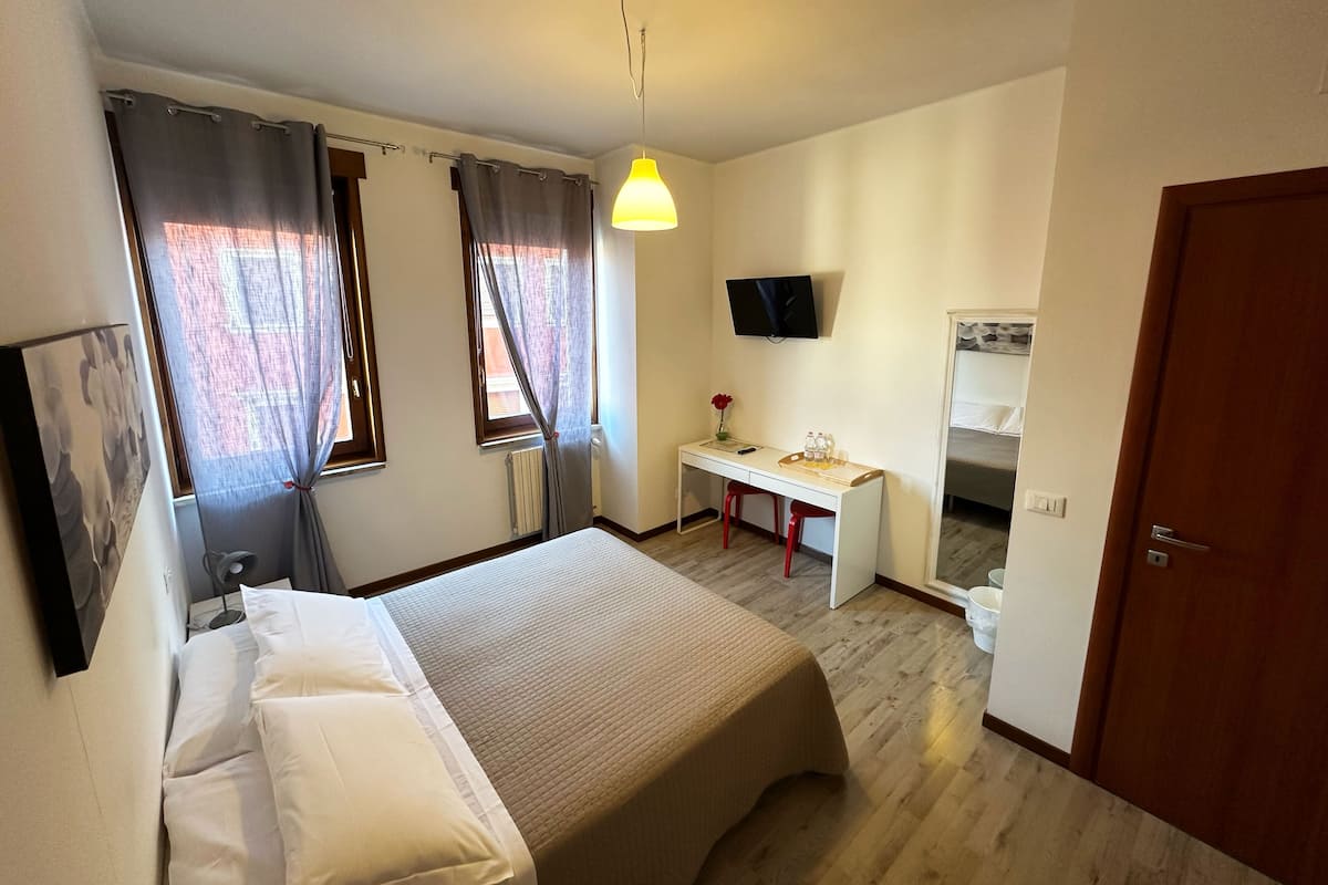A hotel room with a bed, a desk, a chair, a TV, and a door.