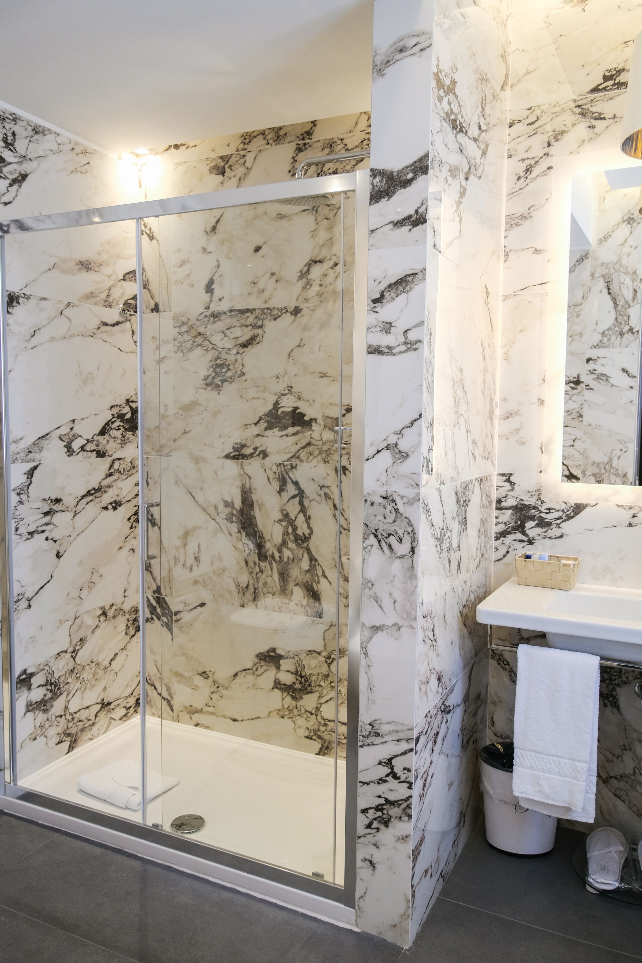 A modern bathroom with a glass-enclosed shower, marble walls, and a white sink with a towel.