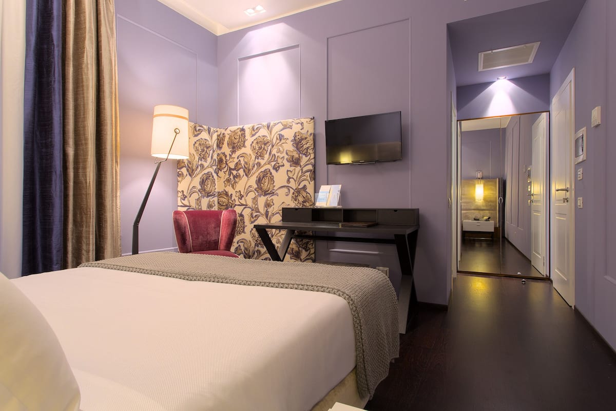 A hotel room with a bed, a desk, a chair, a TV, and a mirror.