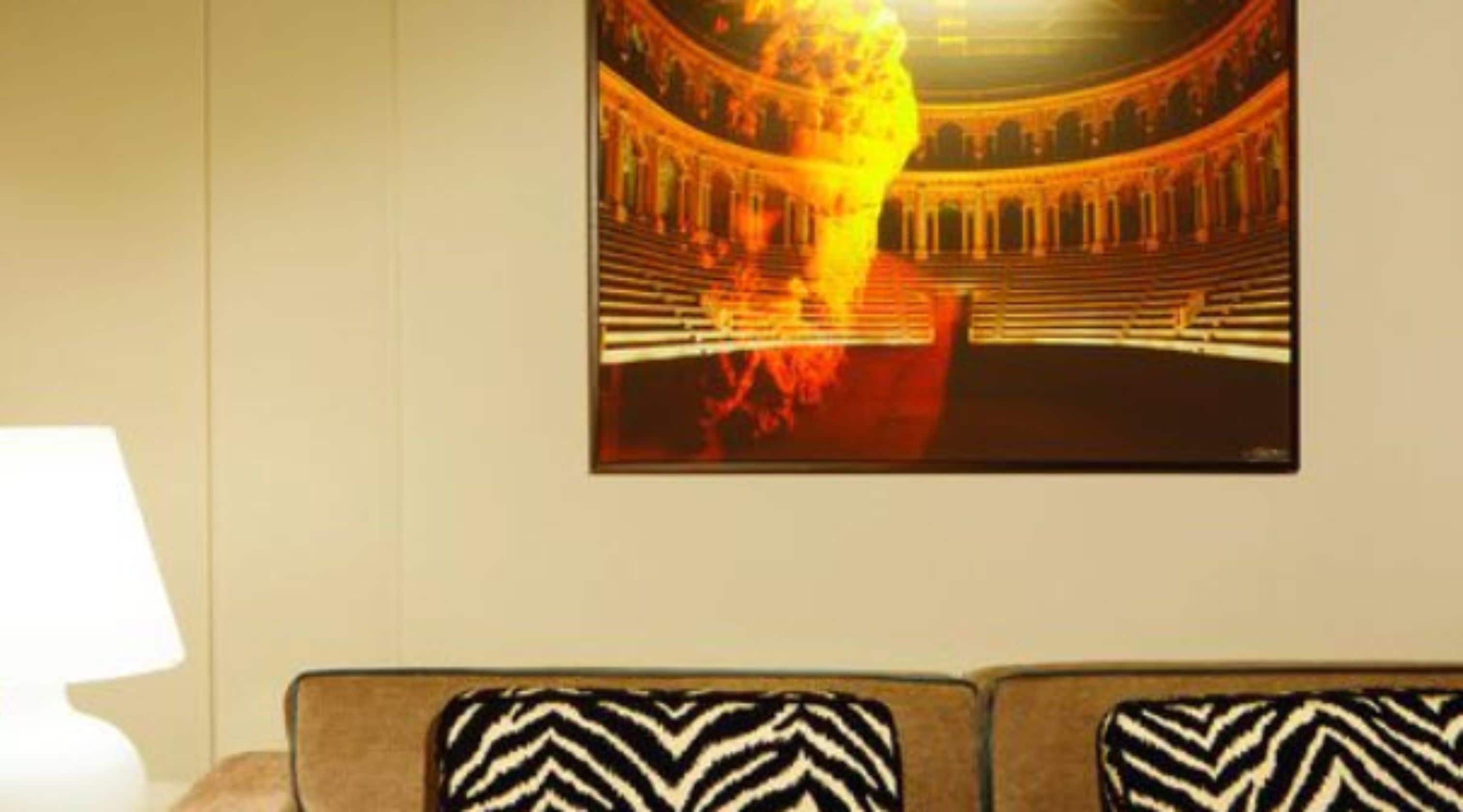 A wall-mounted artwork depicting a classical amphitheater with a central flame, set against a plain wall with a sofa below.
