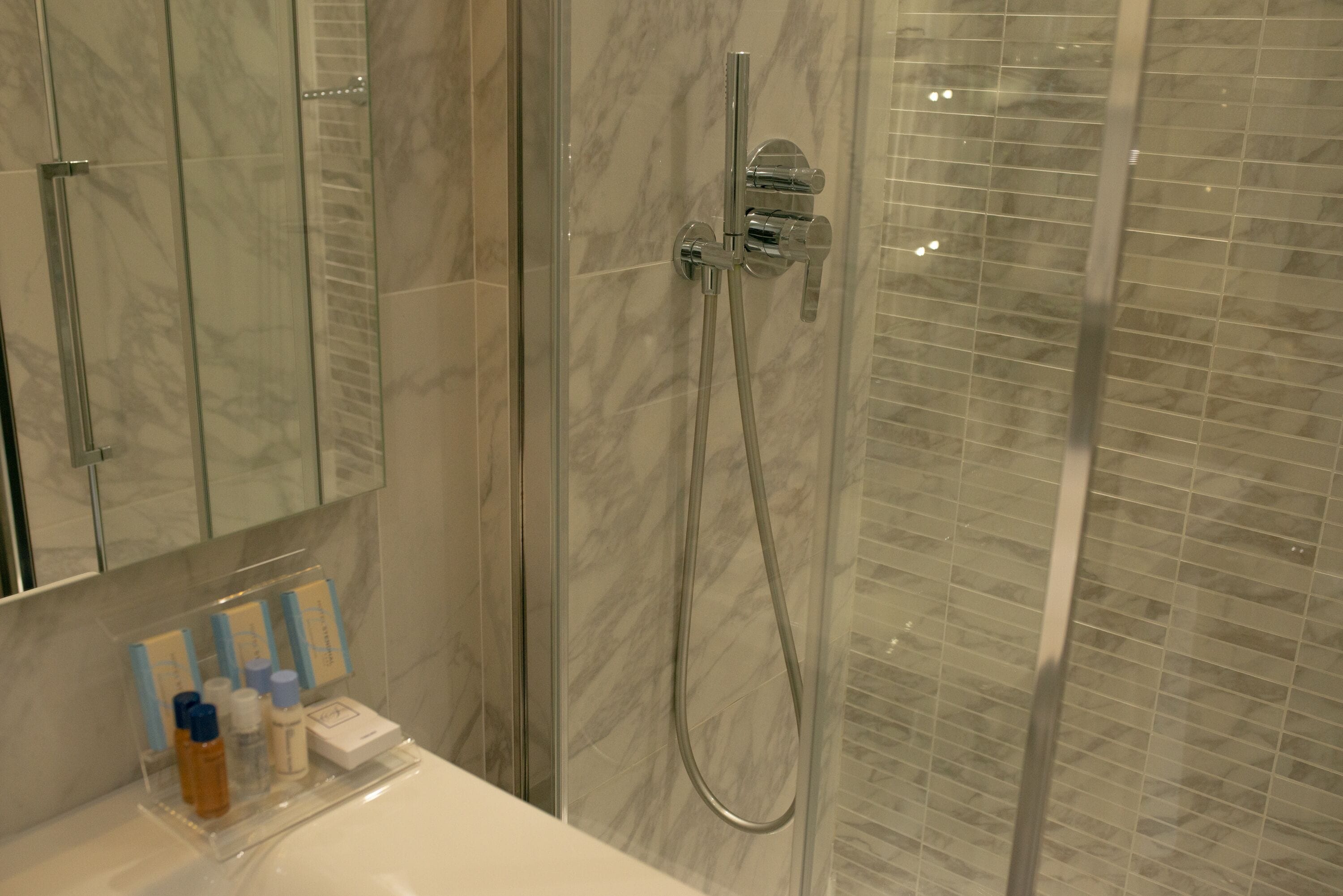 Une salle de bain avec une douche à parois de verre, un lavabo blanc et des articles de toilette posés sur le comptoir.