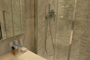 A bathroom with a glass shower enclosure, a white sink, and toiletries on the counter.