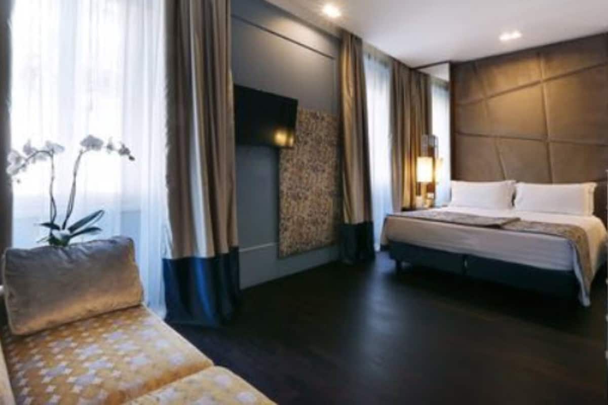 A hotel room with a bed, a sofa, and a large window with curtains.