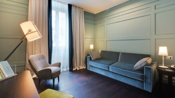 Een kamer met een donkere houten vloer, een blauwe bank, een rieten stoel en twee bedlampen.