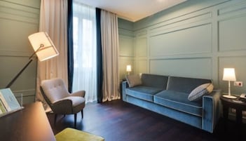 Una stanza con pavimento in legno scuro, un divano blu, una poltrona in vimini e due lampade da comodino.