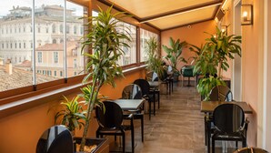 Een lichte ruimte met tafels, stoelen, grote ramen en potplanten.