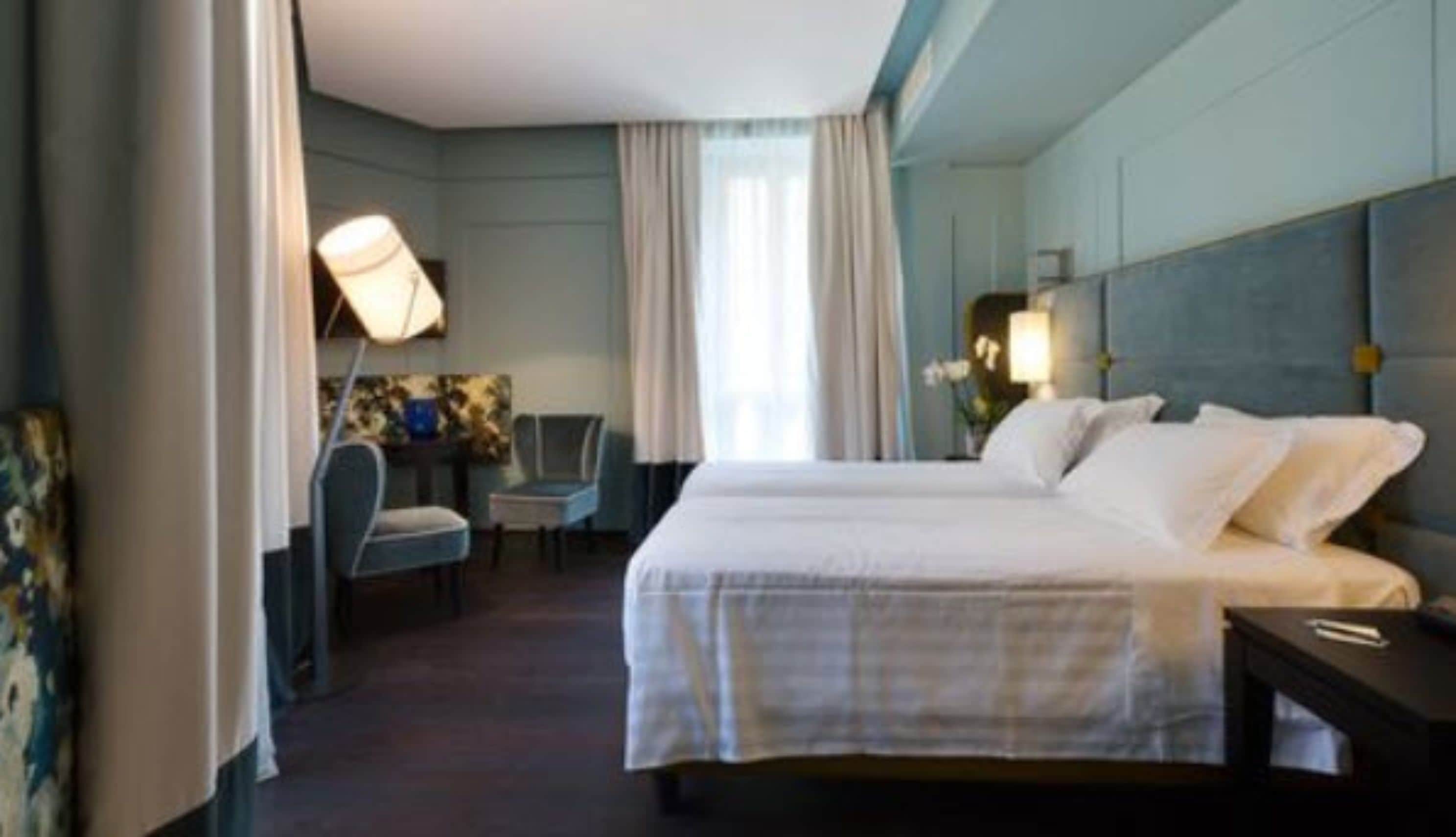 A hotel room with a large bed, two bedside tables, a desk with a chair, and a lamp.