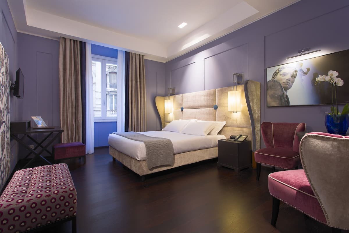 A hotel room with a large bed, a desk, a chair, and a view of the city.