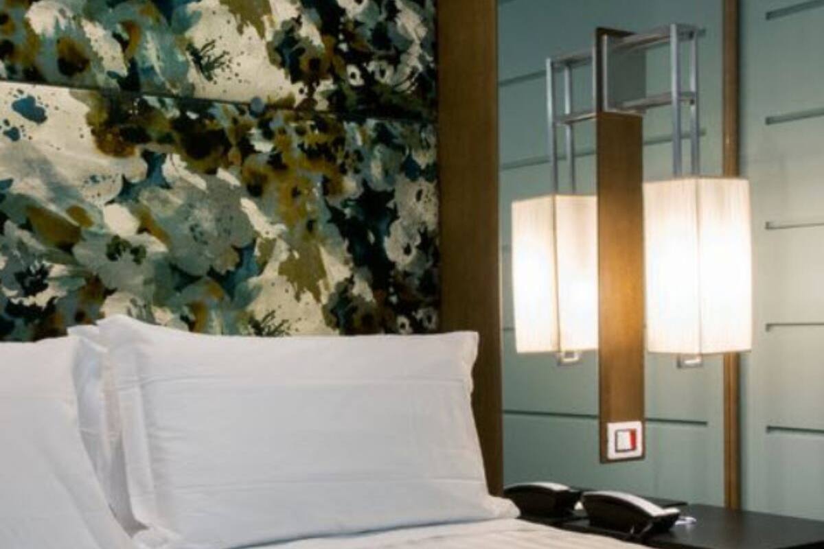 A hotel room with a bed, a nightstand, a lamp, and a floral-patterned wall.