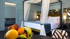 Een hemelbed met witte gordijnen, een nachtkastje met een lamp, en een fruitschaal op een tafel.