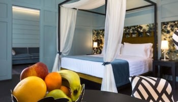 Un letto a baldacchino con tende bianche, un comodino con una lampada e una ciotola di frutta su un tavolo.