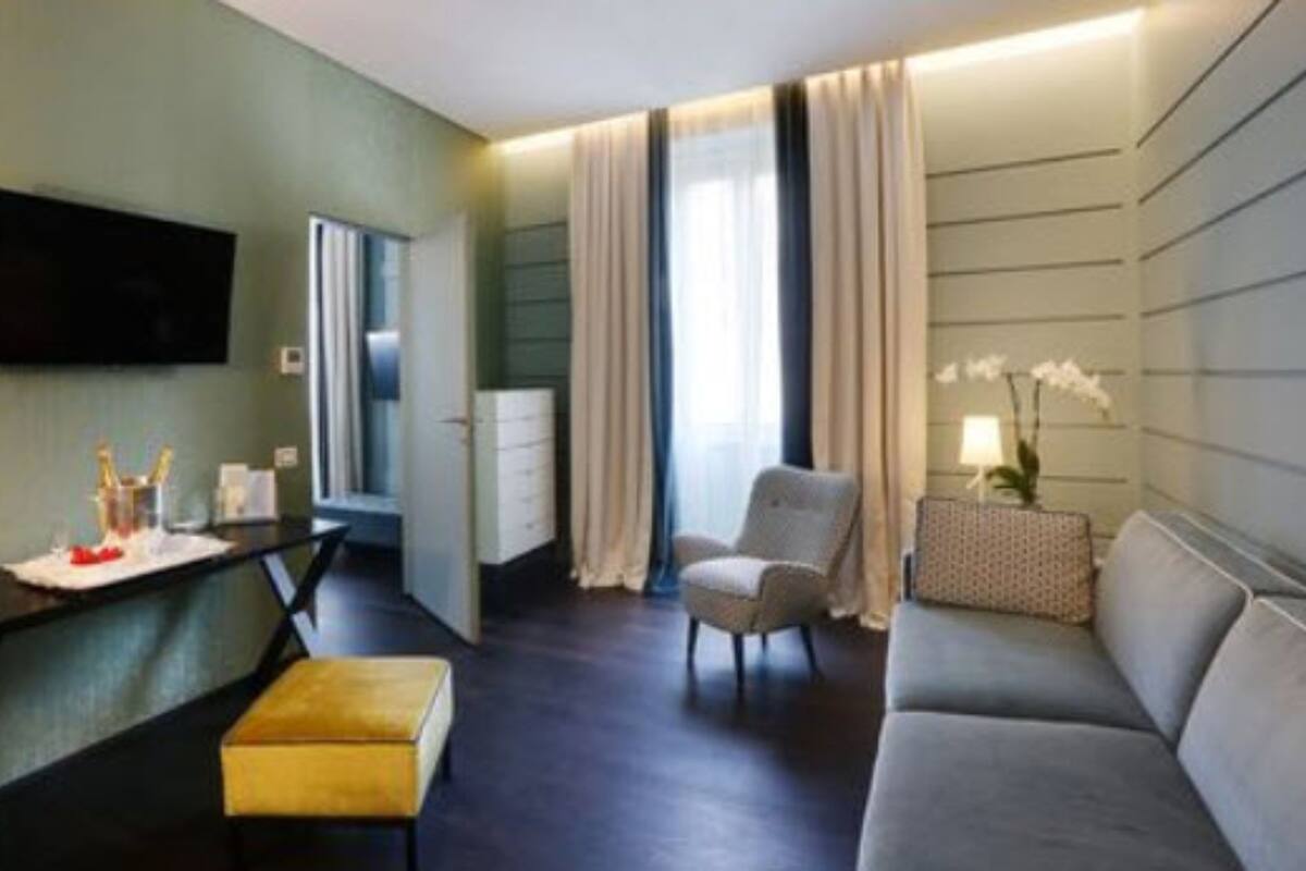 A modern hotel room with a flat-screen TV, a desk with a chair, a sofa, and a small table with a lamp and orchid.