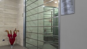 Een moderne hotellobby met een glazen scheidingswand, een rode paraplubak en een bord met de aanduiding van de locatie van het hotel en de suites.