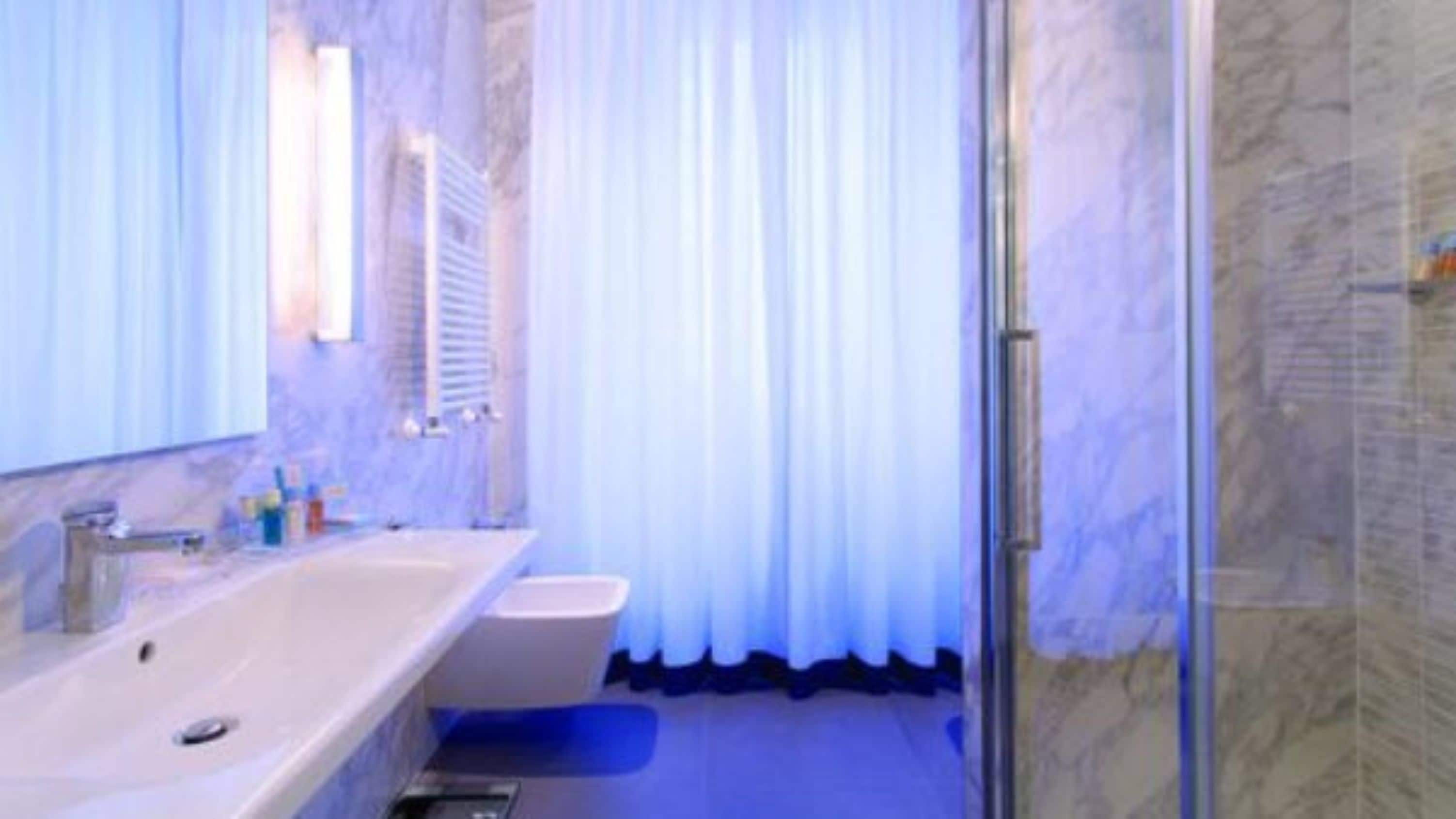 A bathroom with a marble wall, a sink, a mirror, and a shower area.