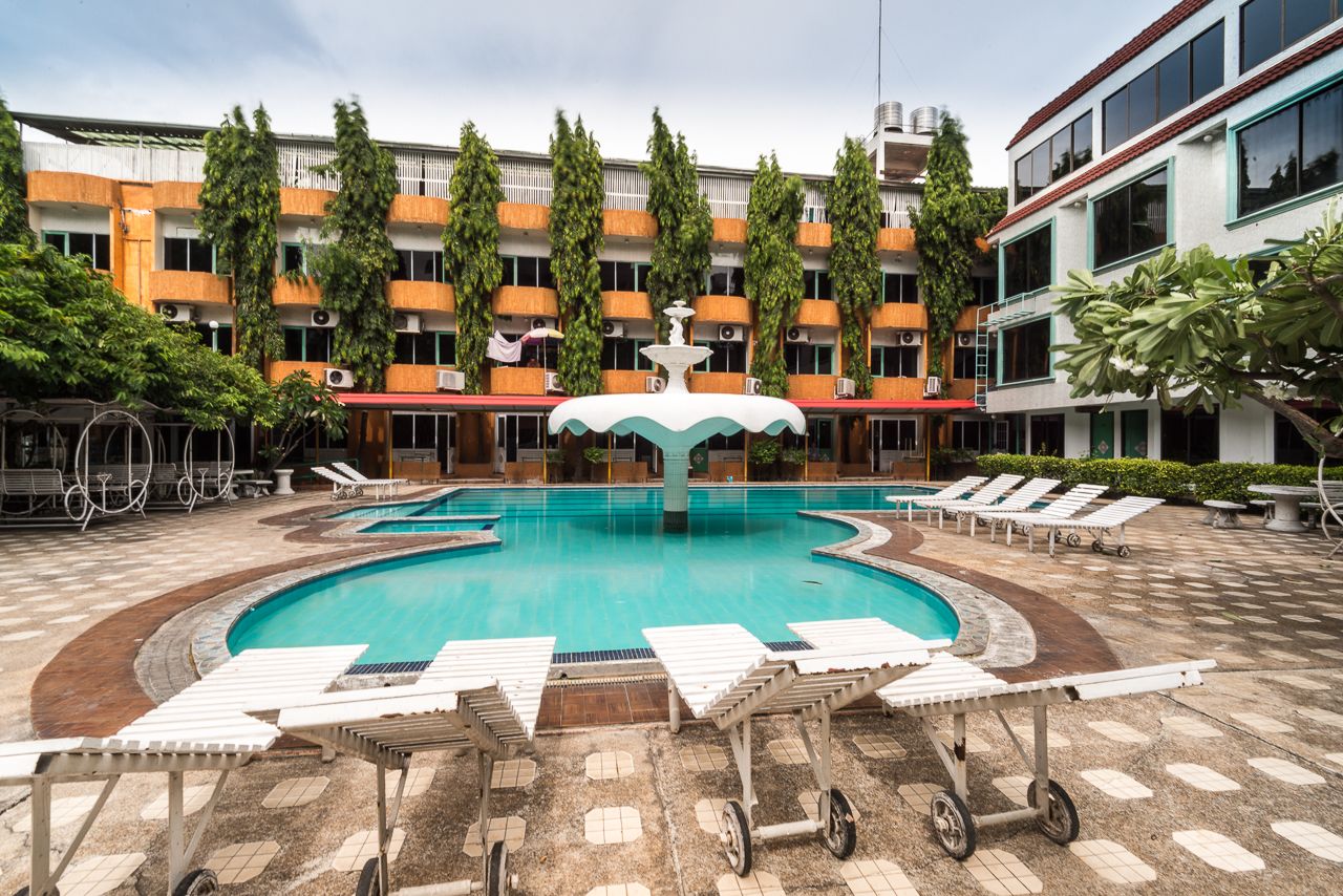 A swimming pool with lounge chairs, surrounded by a building with multiple balconies and trees.