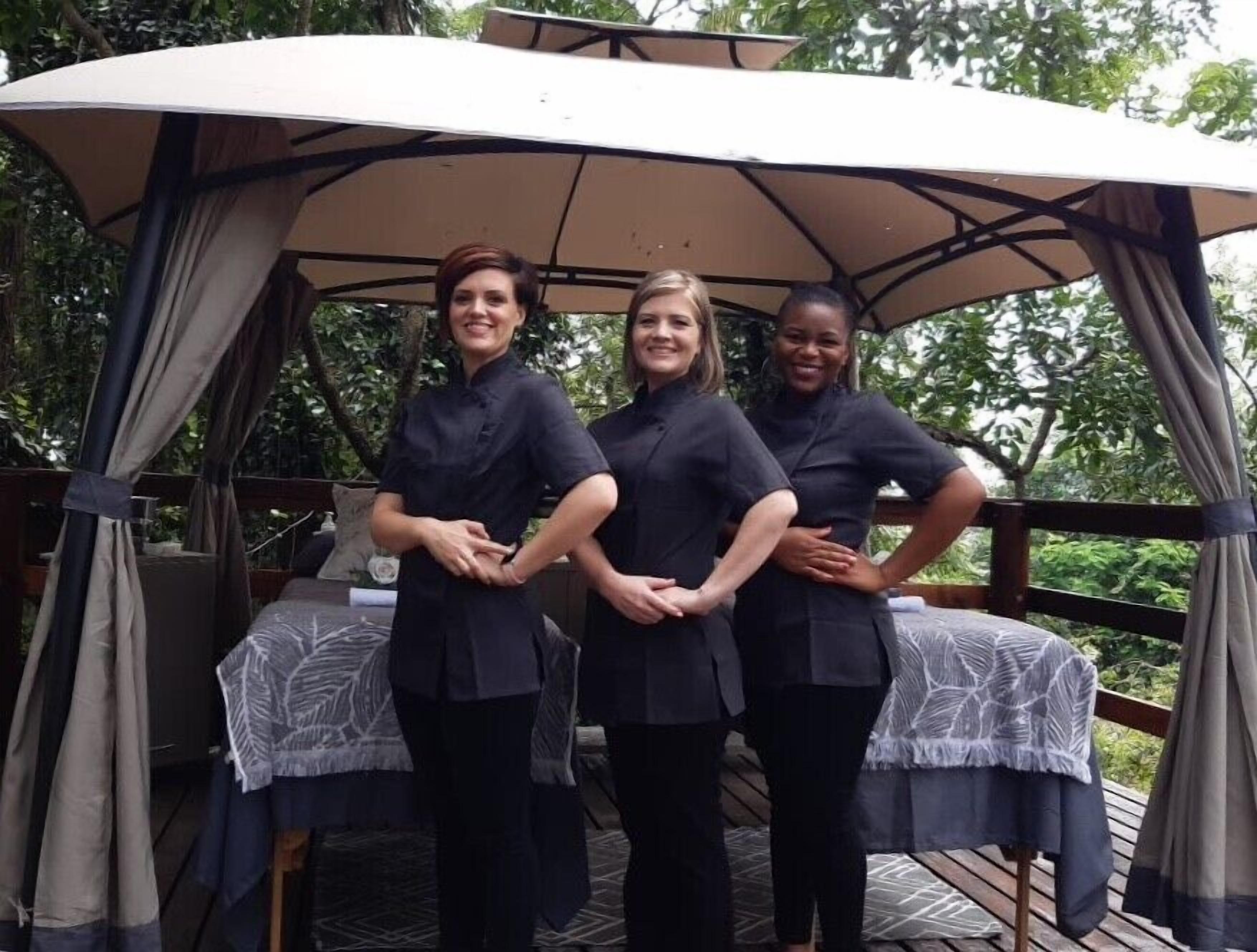 Trois personnes se tiennent sous une marquise sur une terrasse en bois, avec une table et des chaises en dessous.