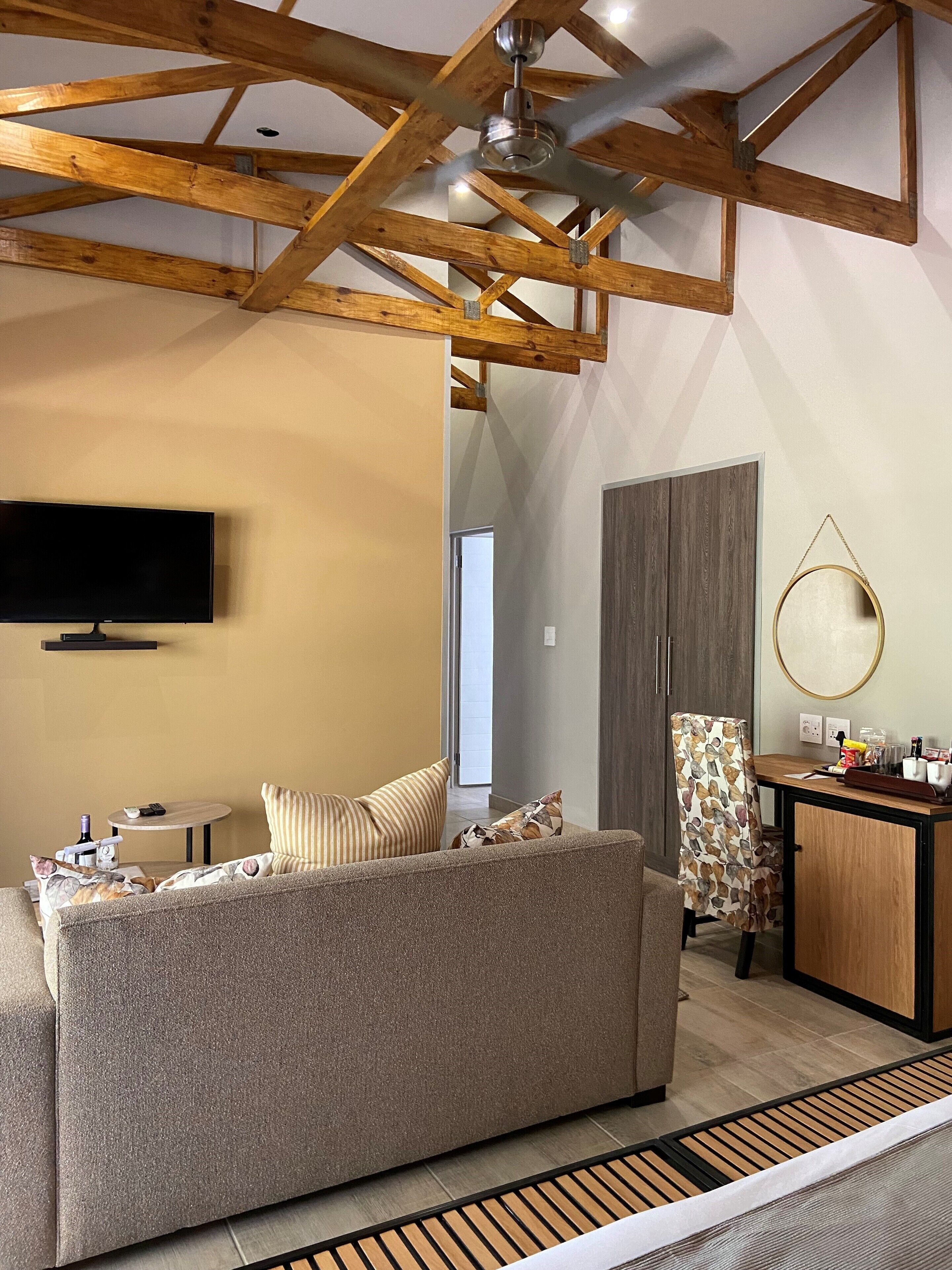 Un salon moderne avec un canapé, un téléviseur, un plafond en bois et un coin cuisine comprenant un meuble et un miroir rond.