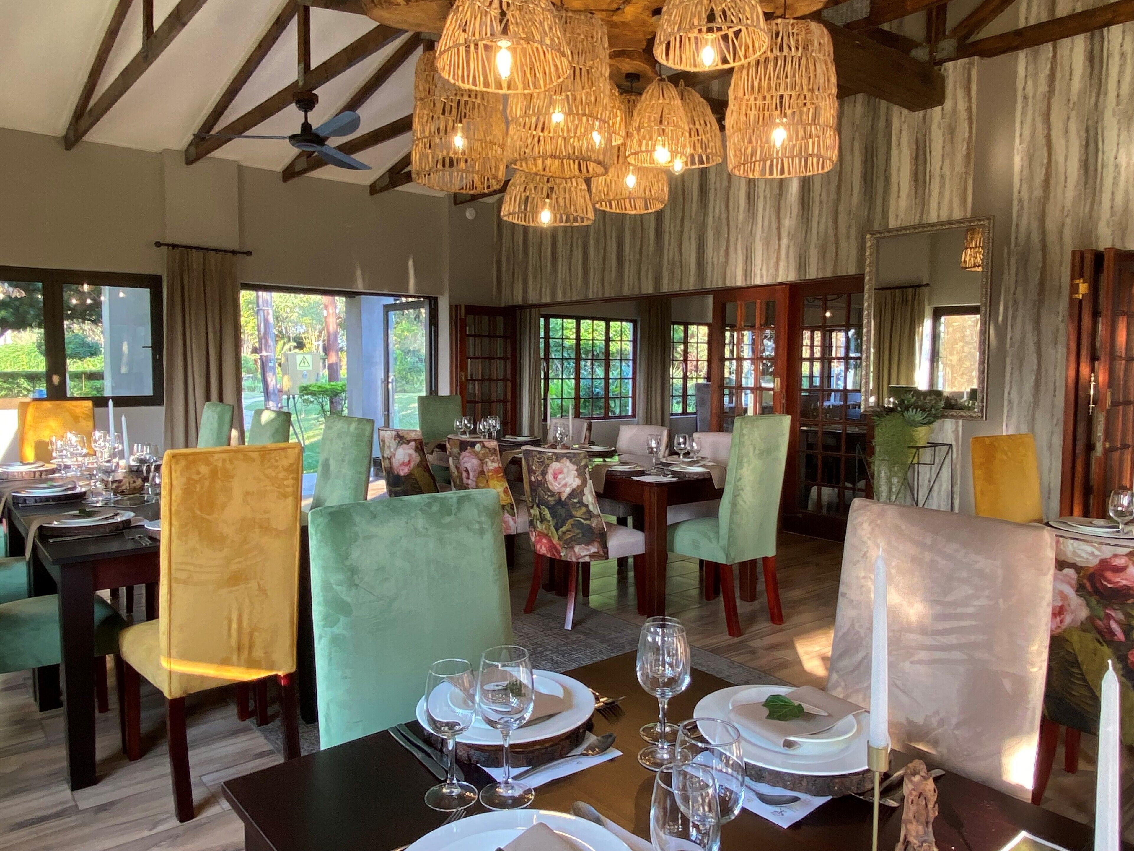 A dining area with tables set for two, featuring green upholstered chairs and a wooden ceiling with exposed beams.