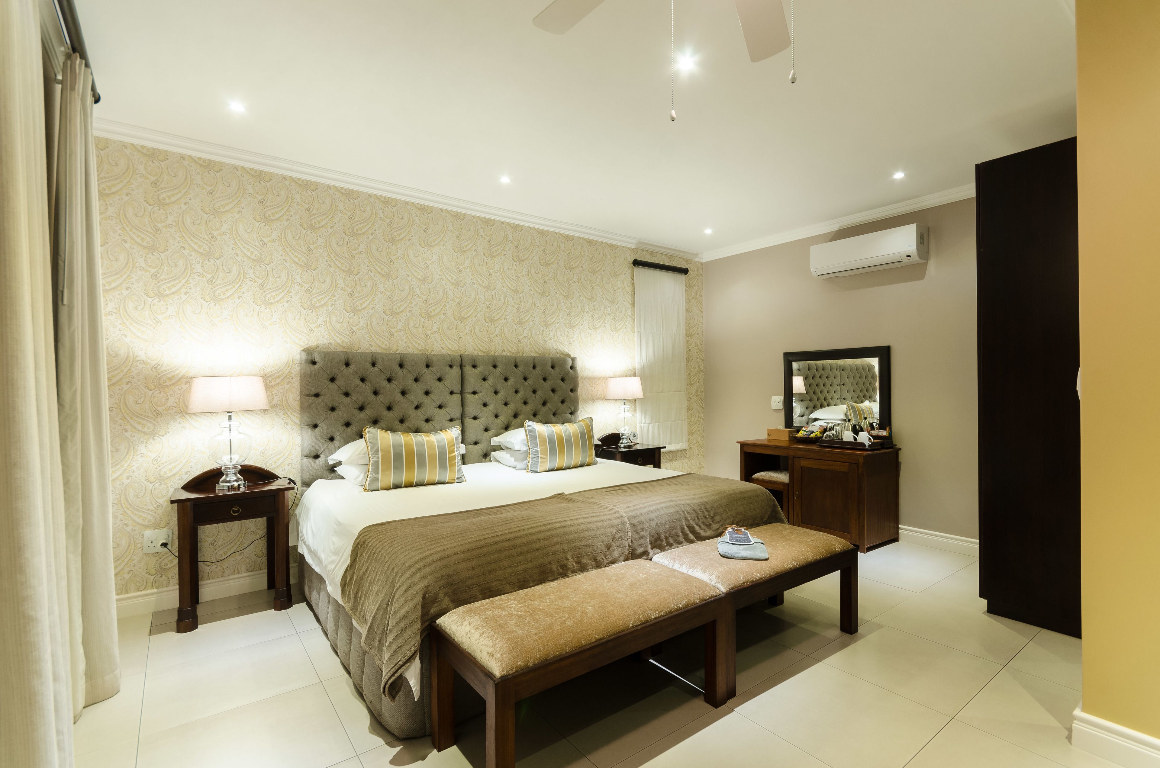 A hotel room with a large bed, two bedside tables, a bench, and a mirror on the wall.