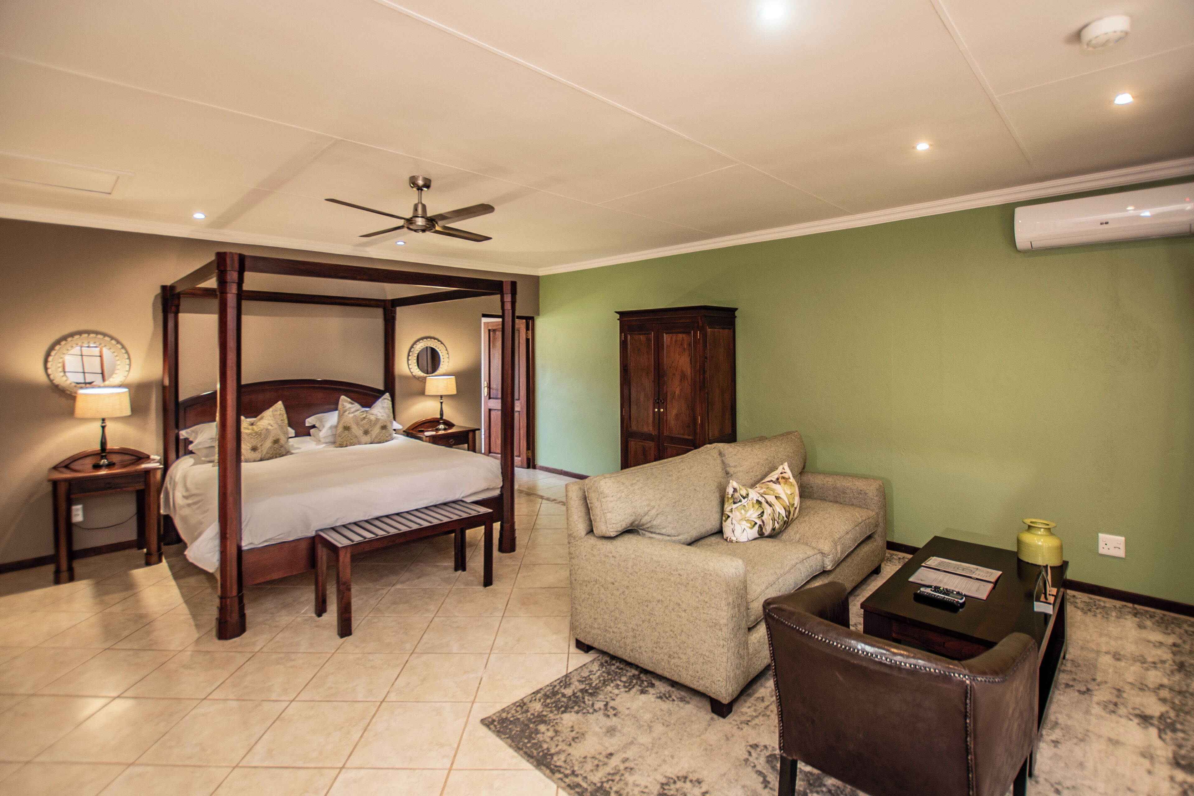 A bedroom with a four-poster bed, a sofa, a coffee table, and a cabinet.
