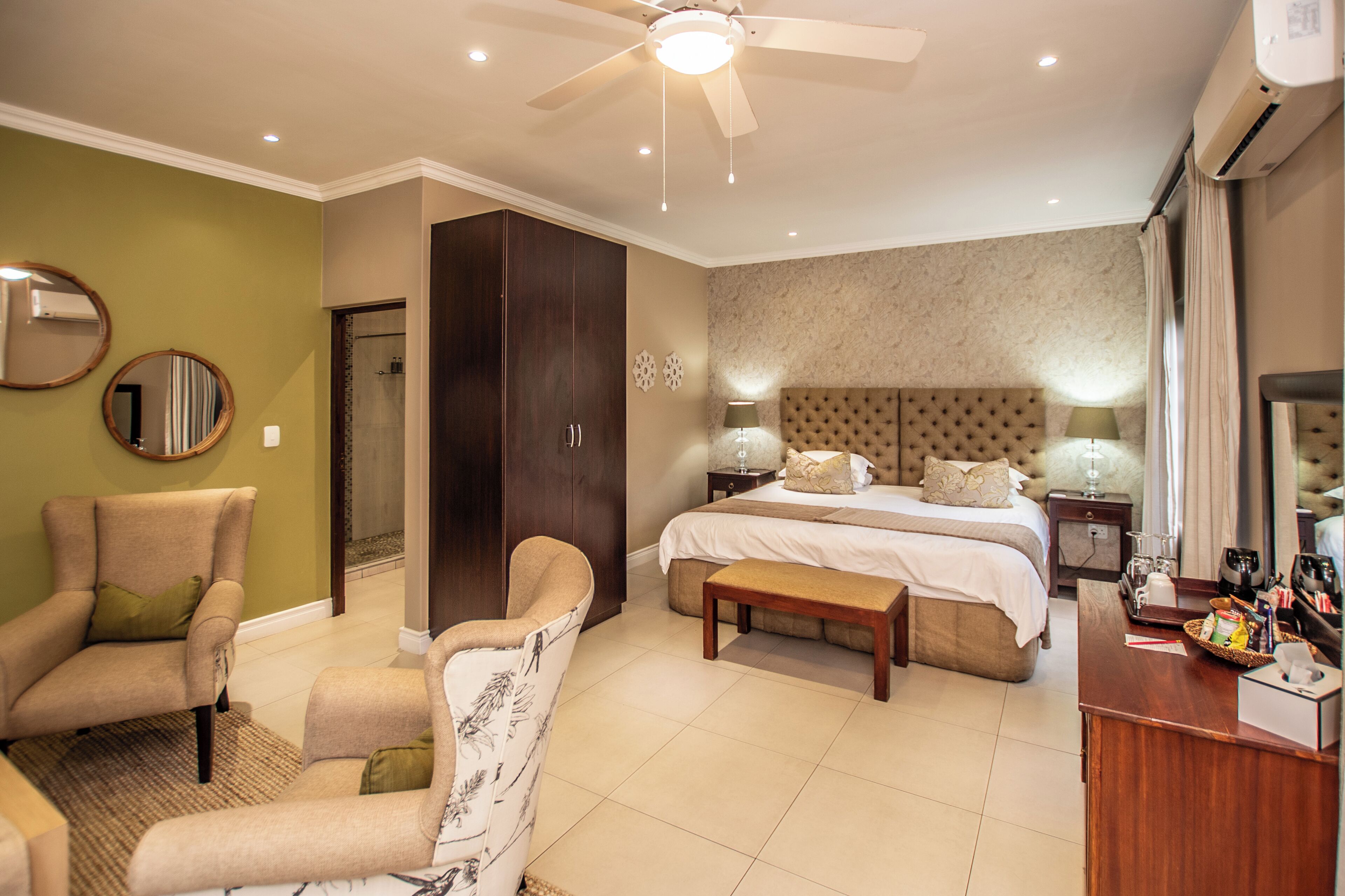 A well-lit bedroom with a bed, bedside tables, a chair, a desk, and a ceiling fan.