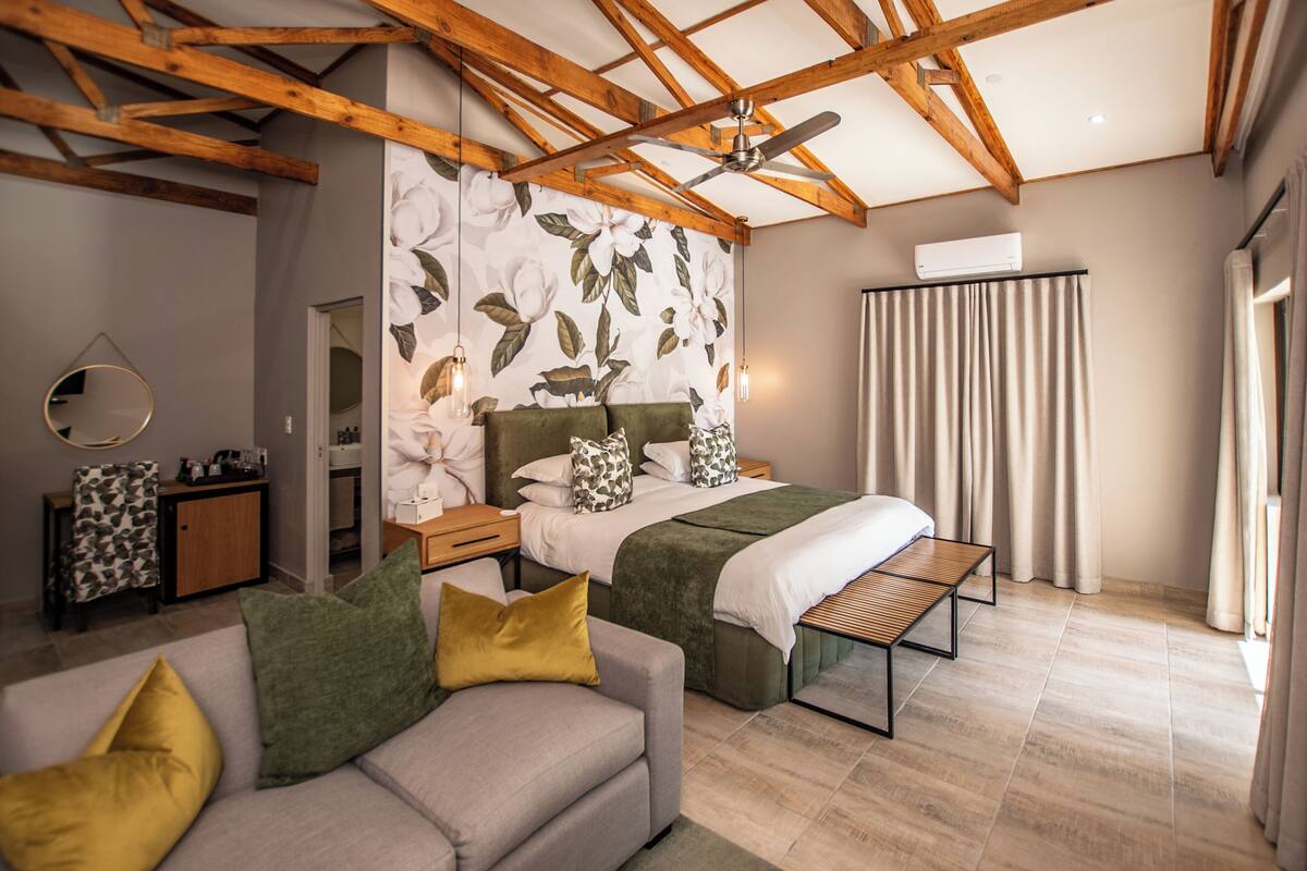 Un dormitorio con cama, sofá, techo de madera y ventana con cortinas.