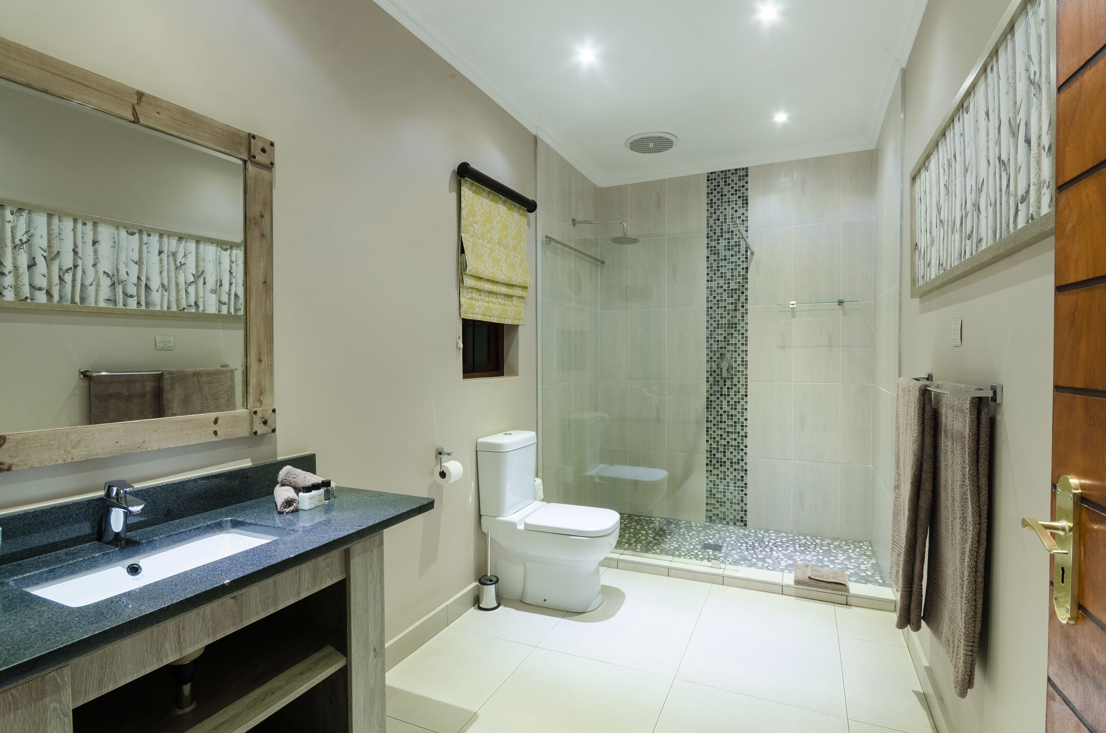 A modern bathroom with a large mirror, a sink, a toilet, and a glass-enclosed shower.