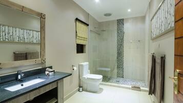 A modern bathroom with a large mirror, a sink, a toilet, and a glass-enclosed shower.