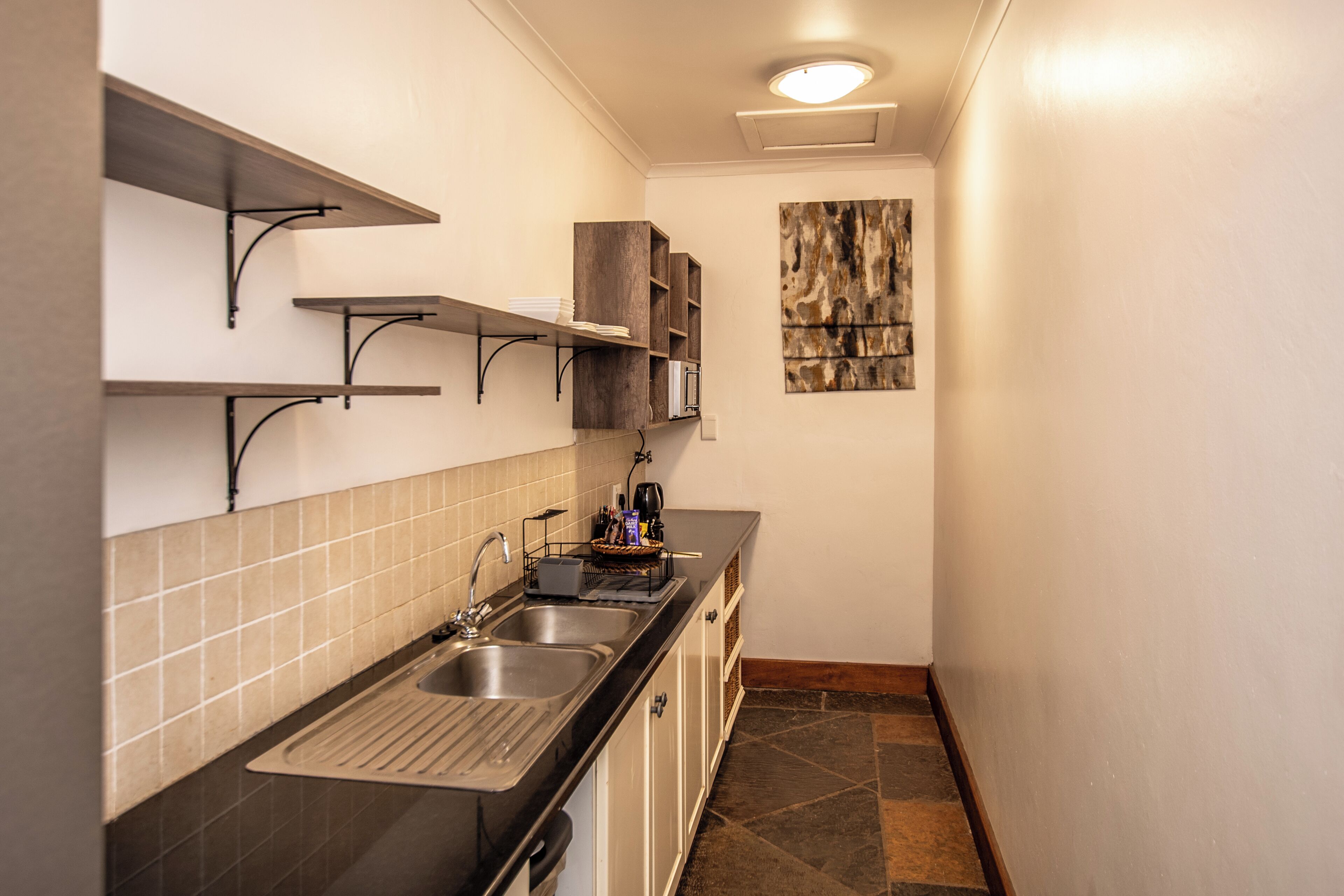 A narrow kitchen with a black countertop, two sinks, and wooden shelves.