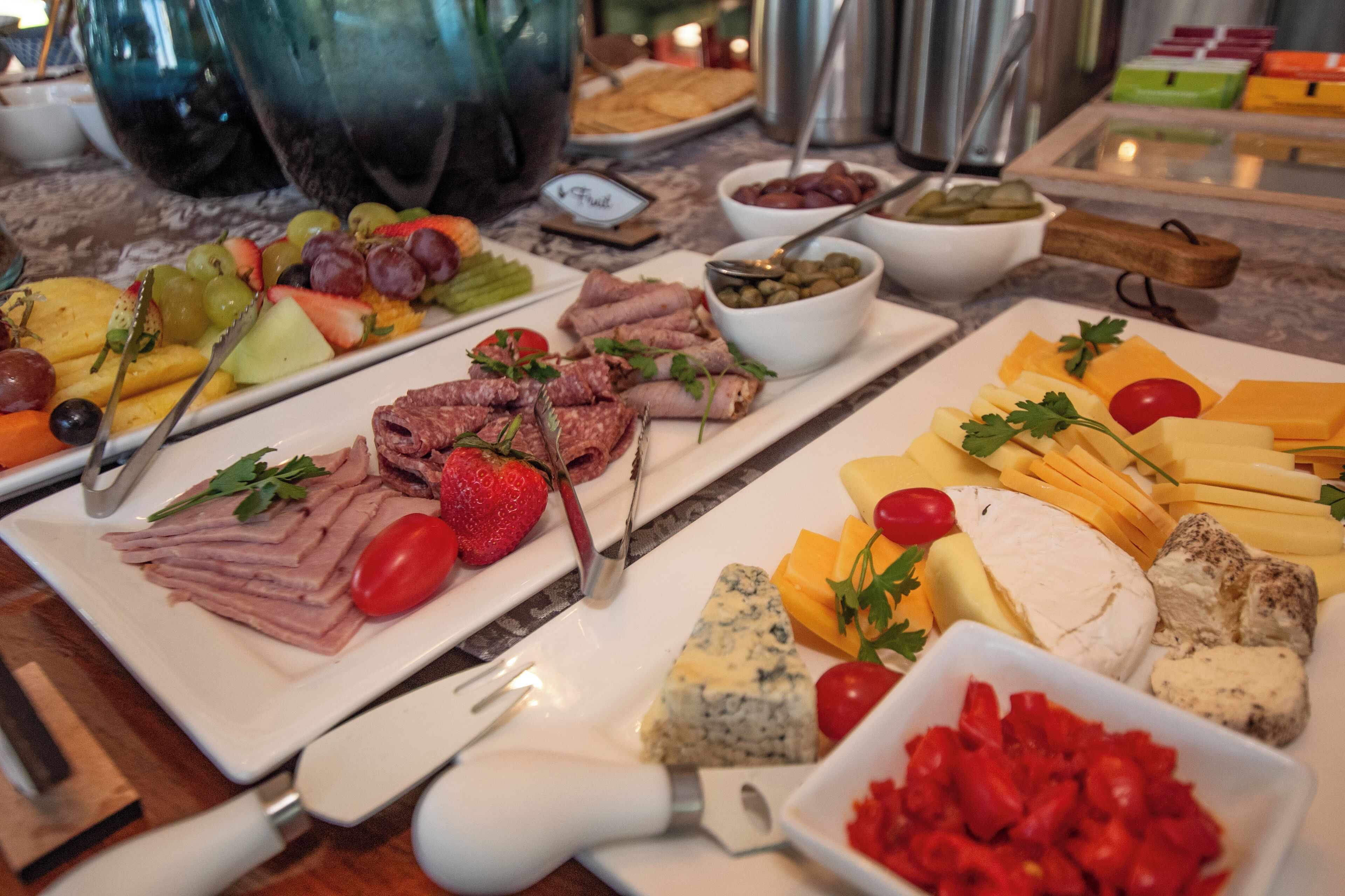 Een buffet met diverse gerechten, waaronder vlees, kazen, fruit en groenten.
