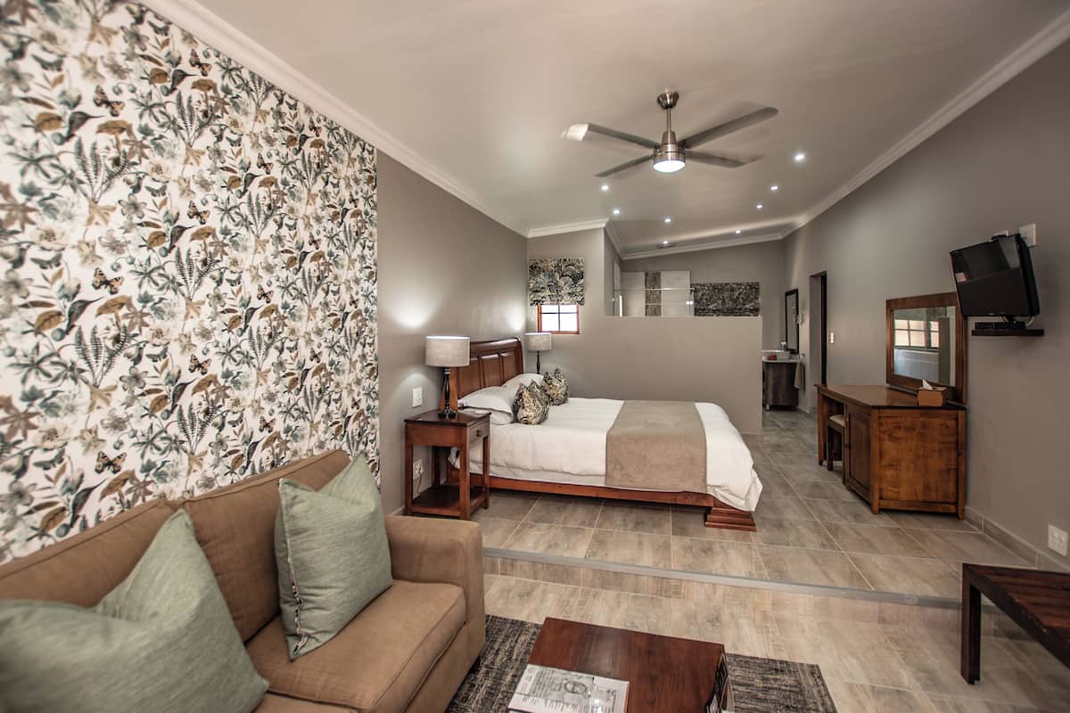 Una habitación de hotel con cama, sofá, televisión y ventilador de techo.