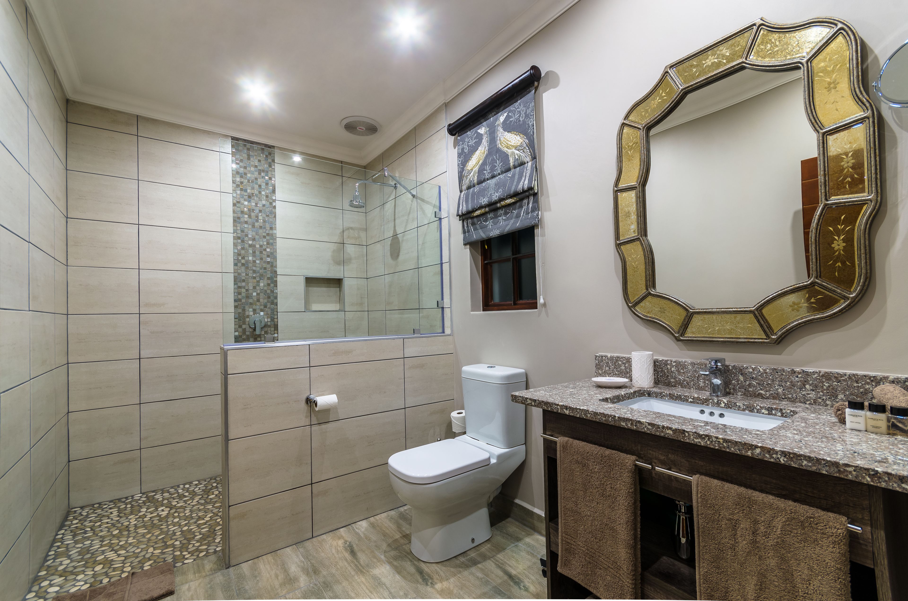 Une salle de bain équipée d’une douche, de toilettes, d’un lavabo et d’un grand miroir agrémenté d’un cadre décoratif.