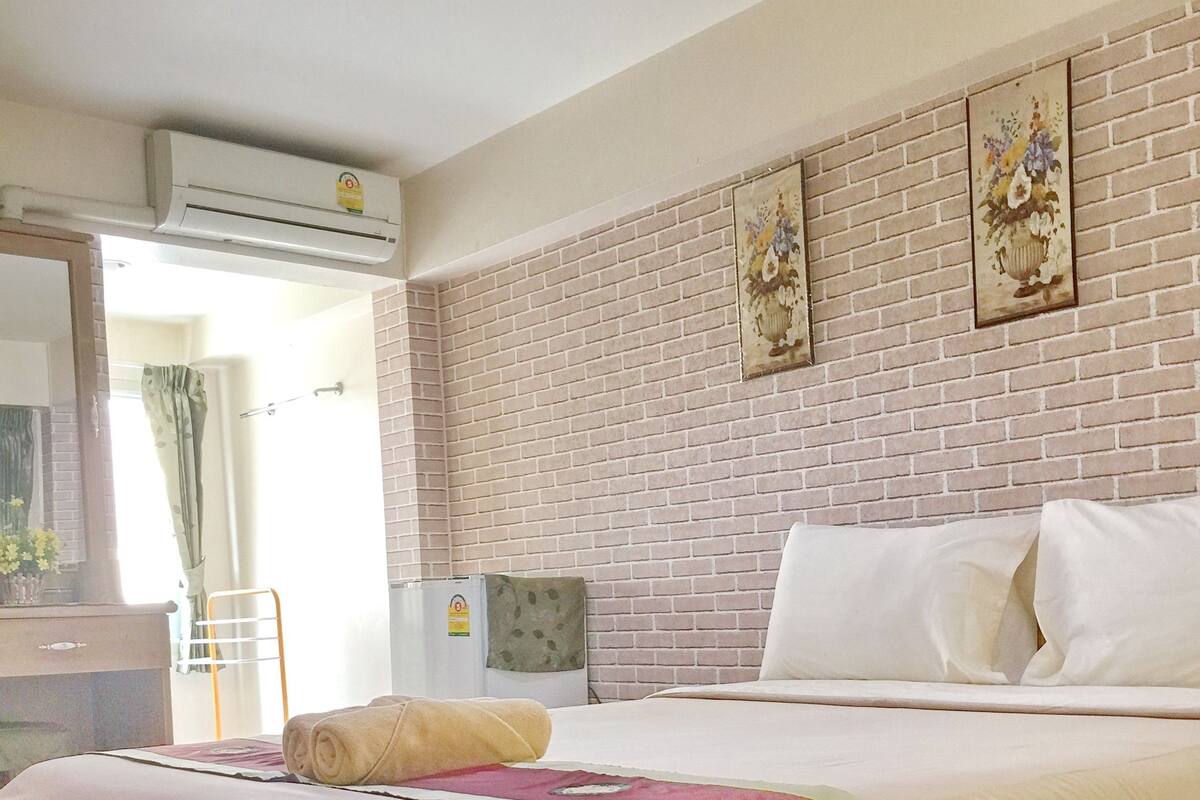 A hotel room with a large bed, a brick-patterned wall, and a window with curtains.