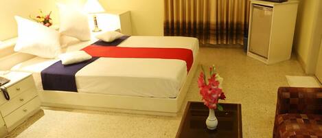 A hotel room with a bed, a nightstand, a desk, a chair, a television, and a vase with flowers.