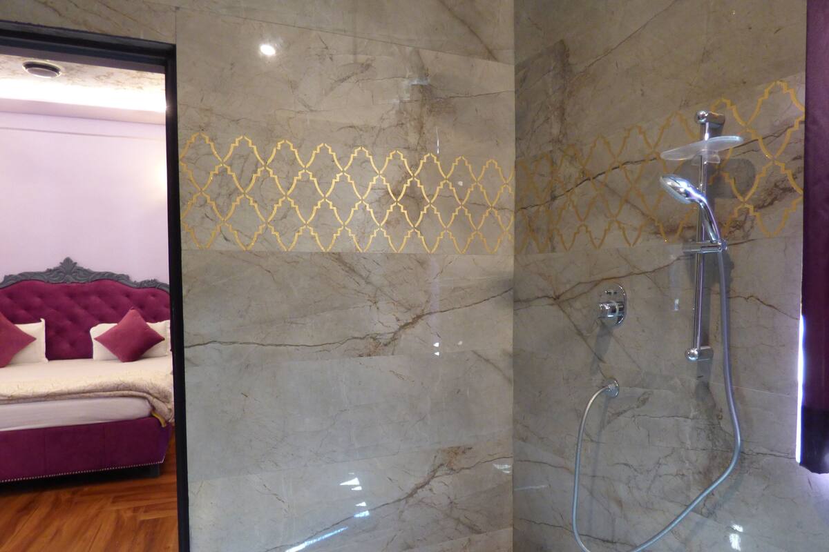A bathroom with a shower, marble walls, and a bed with a purple headboard.