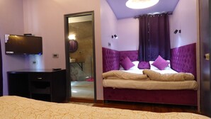 Une chambre à coucher avec un lit, un bureau, une télévision et une salle de bain visible à travers une porte ouverte.