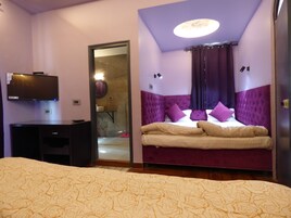 A bedroom with a bed, a desk, a television, and a bathroom visible through an open door.