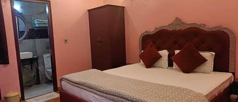A bedroom with a large bed, a wardrobe, a bathroom visible through an open door, and a wall-mounted light fixture.