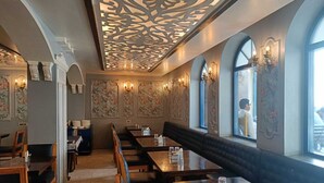 Un restaurant avec des tables et des bancs en bois, des décorations florales sur les murs et des fenêtres en arc de cercle.