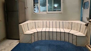 Une cuisine compacte dotée d’un banc incurvé intégré, de deux ventilateurs fixés au mur, d’une fenêtre et d’un réfrigérateur.
