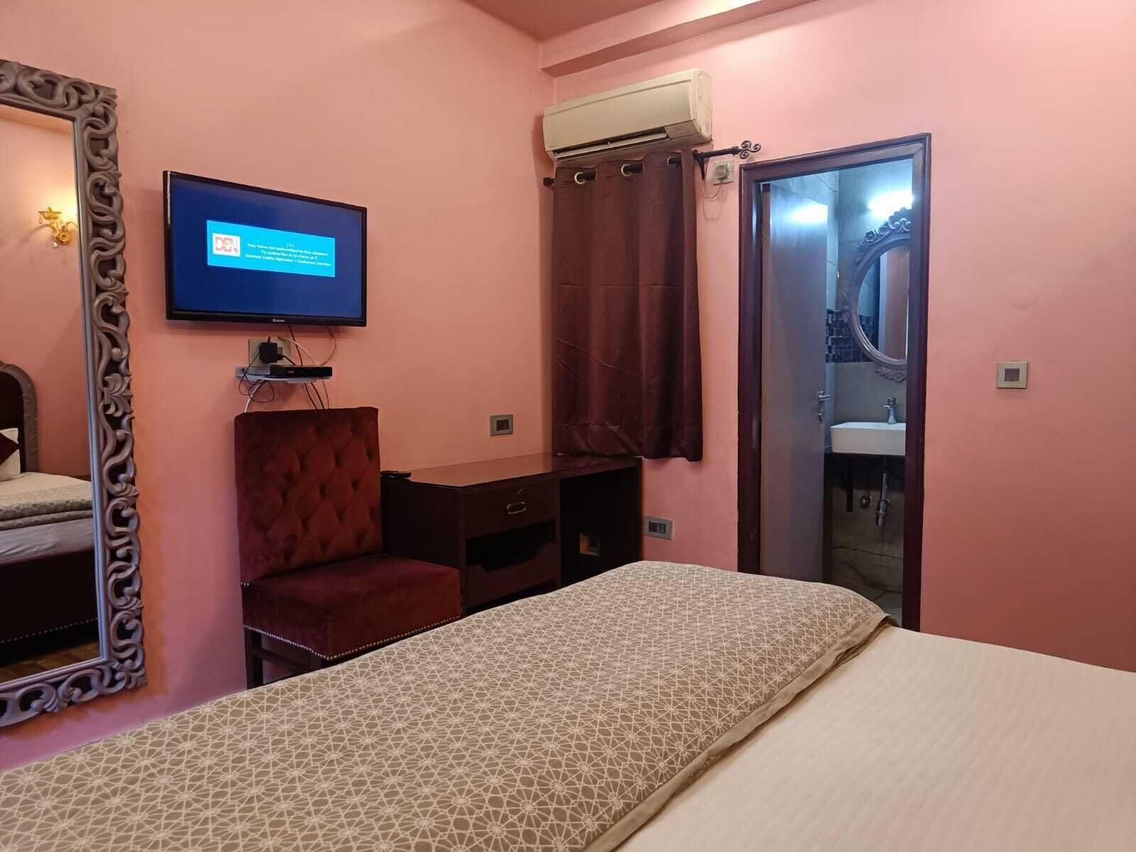 A bedroom with a bed, a TV mounted on the wall, a desk, and a chair.