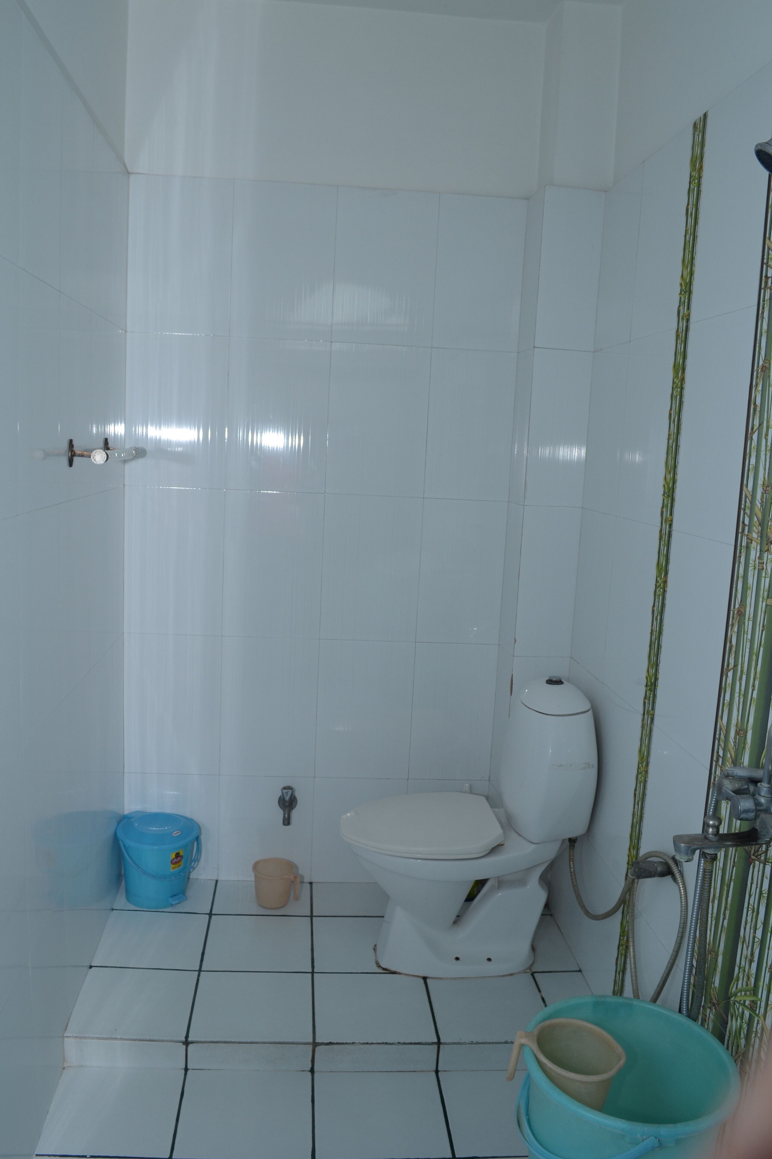 Baño con azulejos blancos, inodoro, lavamanos, un cubo azul y cortina de ducha.