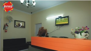A reception area with a reception desk, a television mounted on the wall, a fire extinguisher, a framed picture, and a potted plant. - Innra (Kolkata)