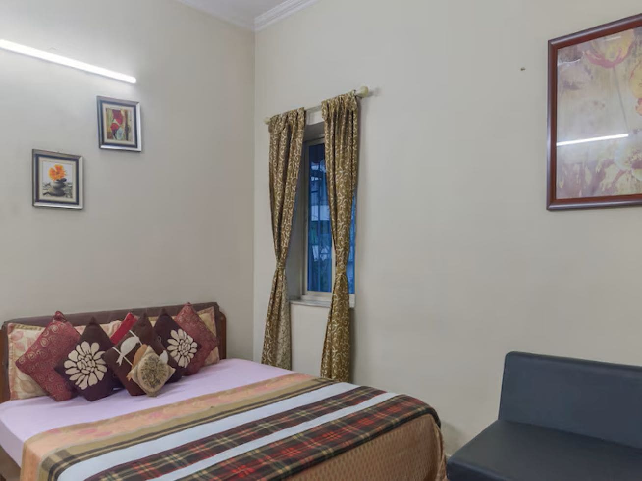 A bedroom with a bed, a window with curtains, a chair, and two framed pictures on the wall.