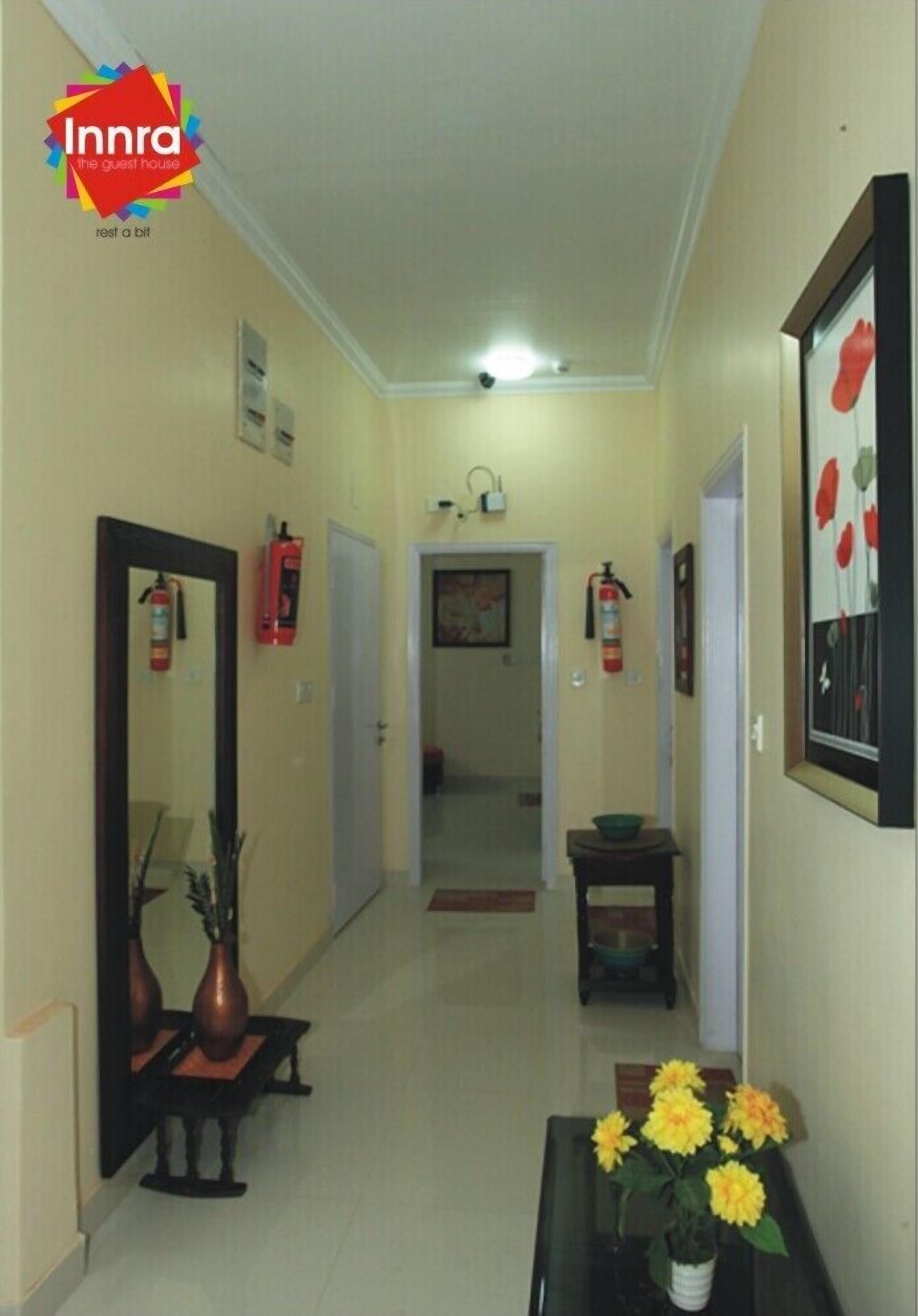A hallway with a mirror, vases, and a framed picture on the walls. There are fire extinguishers mounted on the walls.