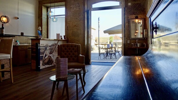 A bar area with a wooden floor, a bar counter, and seating including a tufted armchair and a small round table. - Hotel Poveira (Porto)