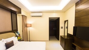 A hotel room with a bed, a TV, a desk, and an air conditioning unit. - Rose wood Residence (Dhaka)