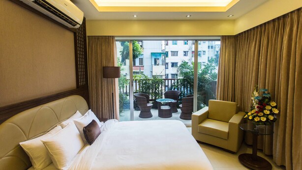 A hotel room with a large bed, a sofa, a small table, and a balcony with outdoor furniture. - Rose wood Residence (Dhaka)
