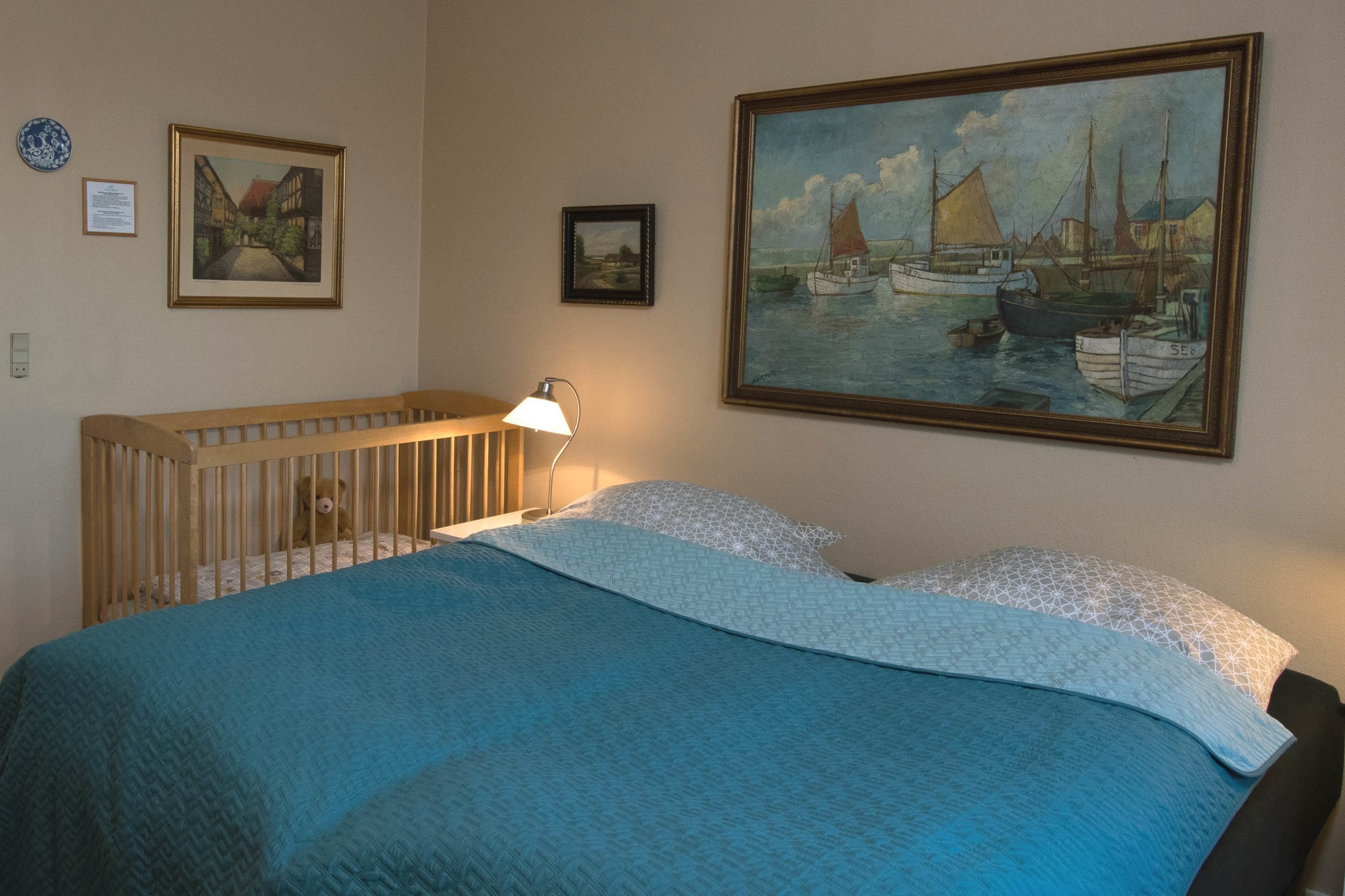 Une chambre avec un berceau, un tableau représentant des bateaux et une lampe.