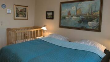 A bedroom with a crib, a painting of boats, and a lamp.